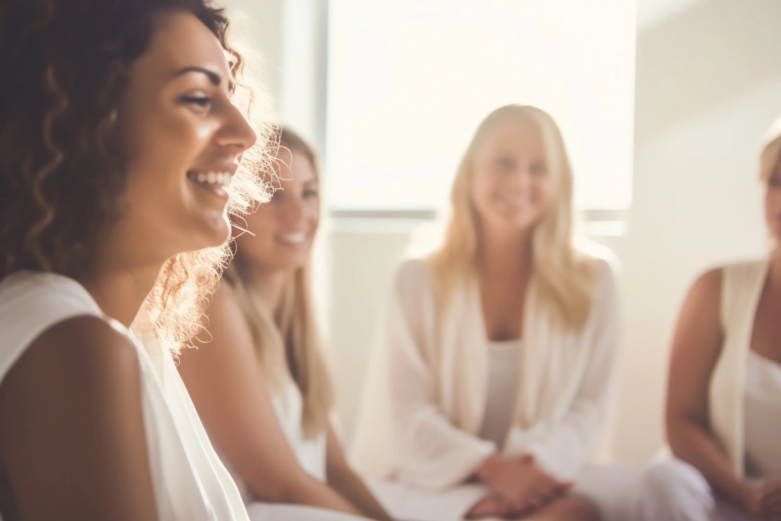 A group of women, dressed in white engaged in a thoughtful discussion in a bright softly lit room A group of women, dressed in white engaged in a thoughtful discussion in a bright softly lit room